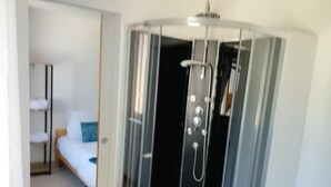 Habitación de esquina con cama, una mesita y cabina de ducha.