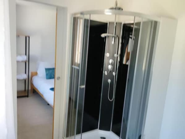 A corner room with a bed, a small table, and a shower enclosure.