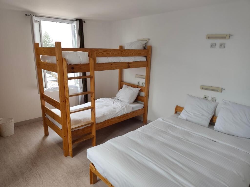 A bunk bed room with a window, a single bed, and a wall-mounted light fixture.