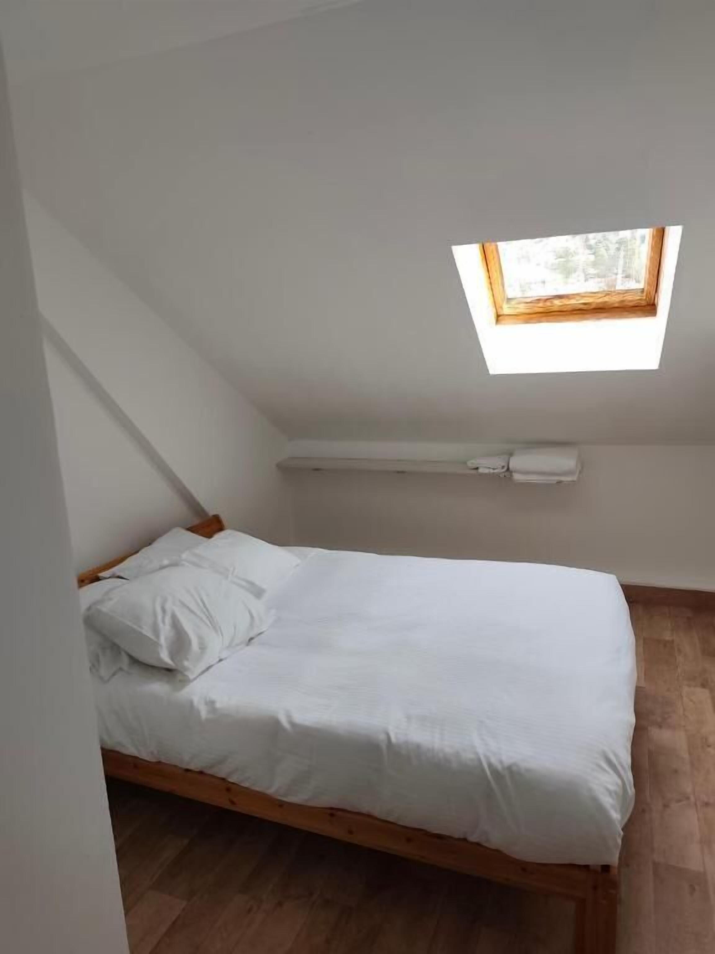 A small, single-bed room with a sloped ceiling and a skylight.