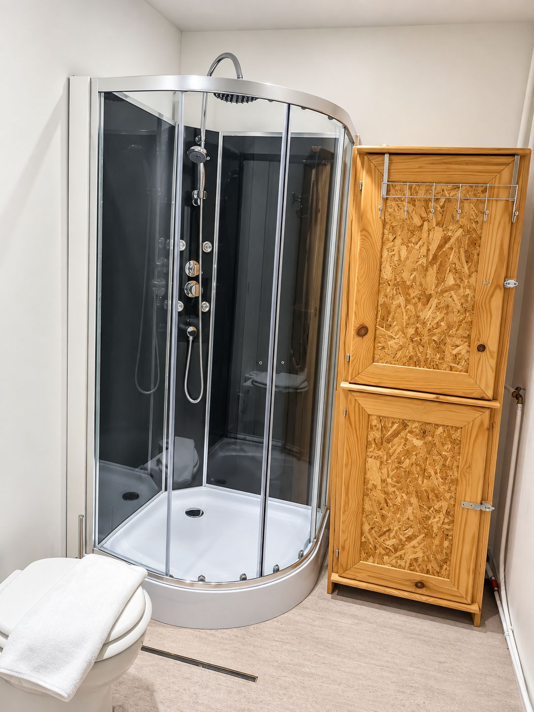 Een douchecabine met een glazen deur, een toilet en een houten kastje.