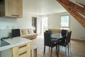 A modern kitchen with wooden cabinets, a dining area with a glass table and chairs, and a view through a door to an outdoor area. - Ice Rock Brasil - Hôtel et restaurant Brésilien (L'Argentière-la-Bessée)