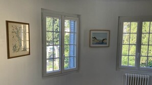 Una habitación con dos ventanas, un radiador y dos cuadros en la pared.
