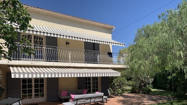 Una casa de dos pisos con un balcón, un patio con mobiliario exterior y un jardín bien cuidado.