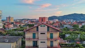 A multi-story building with balconies, surrounded by other residential buildings and a mountainous backdrop. - Cozy 3-bedroom duplex. (Shkodër)