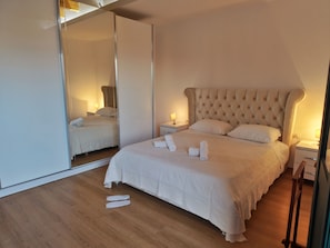 A modern bedroom with a large bed, a mirror, bedside tables, and a wooden floor. - Cozy 3-bedroom duplex. (Shkodër)