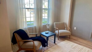 Une piĂšce avec deux chaises, une petite table et une fenĂȘtre avec des rideaux.