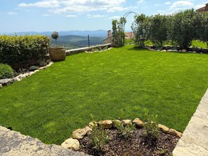A well-maintained lawn with a stone border, a stone planter, and a view of distant hills.