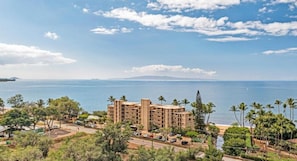 Ein Hotel an der Küste mit mehreren Etagen, einem Parkplatz und Blick auf das Meer und ferne Berge.