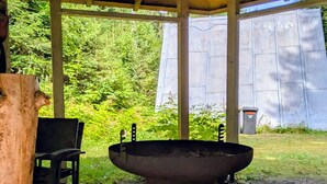 A covered outdoor area with a large metal basin, wooden logs, and a chair. - Cozy hut ''Fuchsbau'' in the middle of the forest. Pet friendly! (Eibenstock)