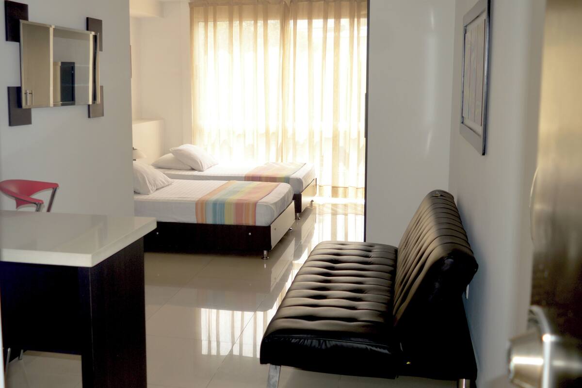 Une chambre d’hôtel avec un lit, un canapé, un bureau et une fenêtre avec des rideaux.