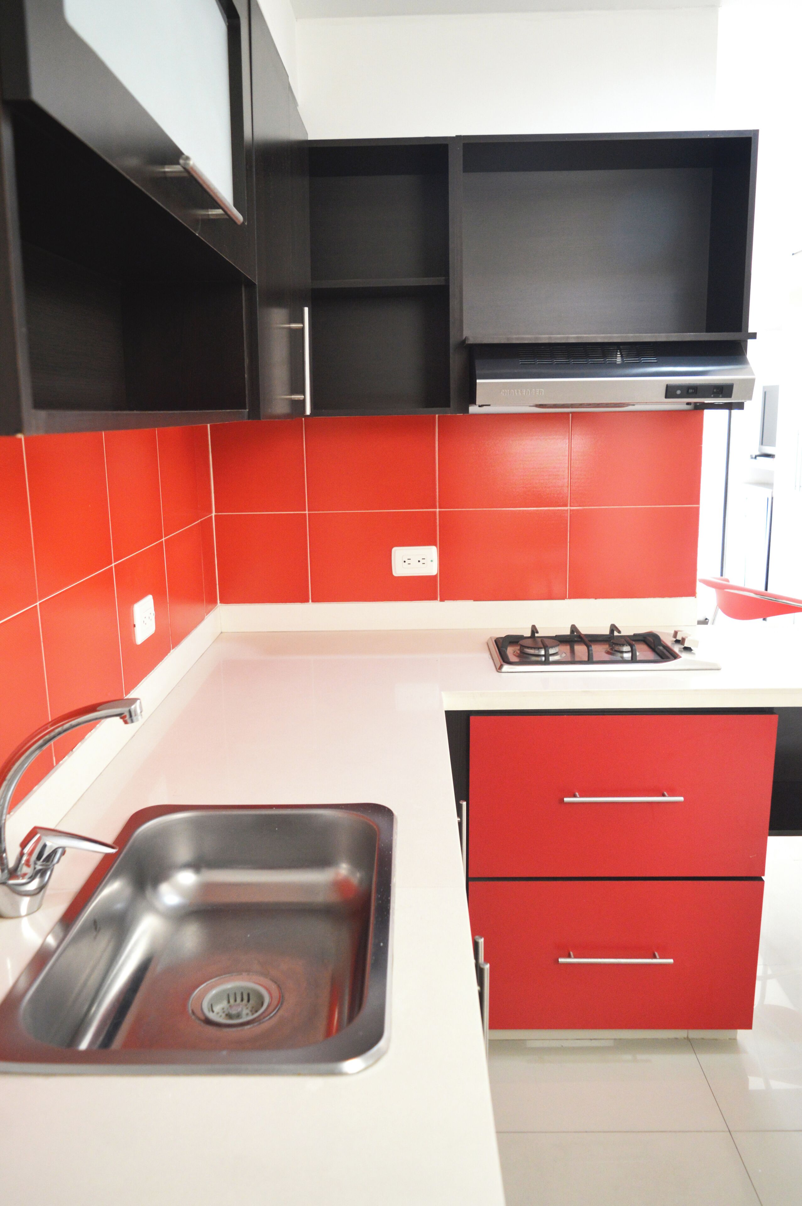 Una cocina con un lavamanos de acero inoxidable, armarios rojos y una estufa a gas.