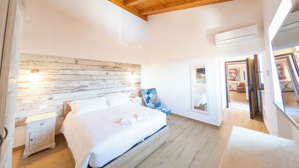 Ein Schlafzimmer mit Holzboden, einem Bett mit weißer Bettwäsche, einem Nachttisch, einem Sessel und einem Spiegel.