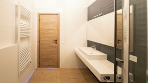 Ein modernes Badezimmer mit Holztür, Waschbecken in Weiß und einer Duschkabine aus Glas.