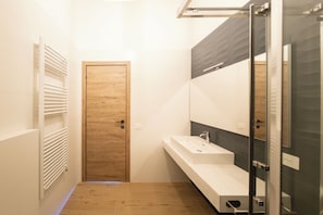 Ein modernes Badezimmer mit Holztür, Waschbecken in Weiß und einer Duschkabine aus Glas.