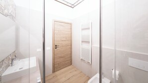 Ein modernes Badezimmer mit Duschkabine aus Glas, einer Holztür, einem weißen Waschbecken und einem weißen Handtuchhalter.