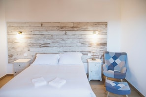 Ein Schlafzimmer mit einem hölzernen Kopfteil, einem Bett mit weißer Bettwäsche, zwei Nachttischen und einem gemusterten Sessel.