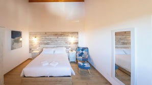 Ein Schlafzimmer mit Holzboden, einem Bett mit weißen Leinentüchern, einem Nachttisch mit Lampe und einem blauen Sessel.