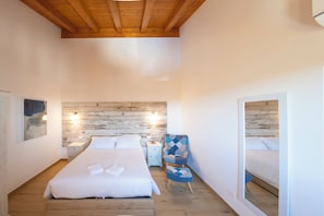 Ein Schlafzimmer mit Holzboden, einem Bett mit weißen Leinentüchern, einem Nachttisch mit Lampe und einem blauen Sessel.