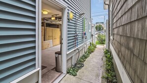Une ruelle étroite avec une entrée d’immeuble, une poubelle visible et un tuyau d’arrosage sur le sol.