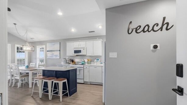 Une cuisine moderne avec des meubles blancs, un îlot central et un coin repas avec des chaises blanches.