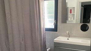 Un baño con cortina de ducha, un lavabo, un espejo y una alfombra oscura.