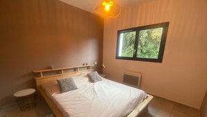 Un dormitorio con una cama de madera, dos almohadas, una mesita de noche, una lámpara, una ventana y un radiador.