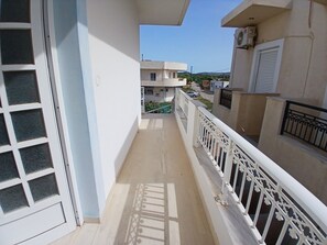 En smal balkon med hvid gelænder, en glasdør og udsigt til omkringliggende bygninger.