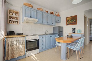 A kitchen with blue cabinets, a stove, a refrigerator, and a dining table with chairs. - Apartment 'Memories' with Balcony, Wi-Fi and Air Conditioning (Palekastro)