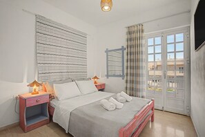 Ein Schlafzimmer mit einem Bett, Nachttischen, einer Lampe, einem Fenster mit Vorhängen und Blick auf Gebäude.