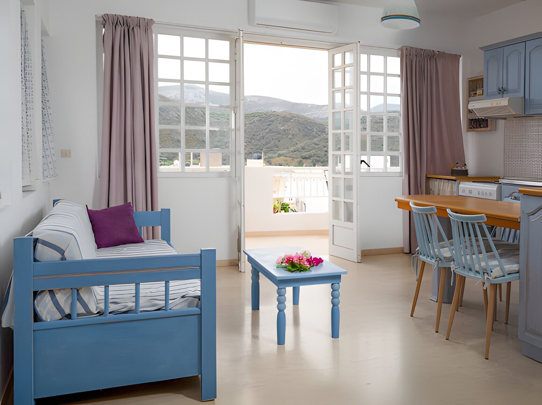 A room with a bed, a table with flowers, a kitchen area, and a balcony with a view of the mountains.. Apartment 'Memories' with Balcony, Wi-Fi and Air Conditioning