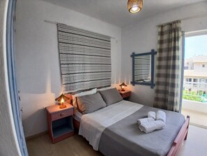 Camera d'albergo con un letto, comodini, una lampada, una finestra con tende e vista sugli edifici.