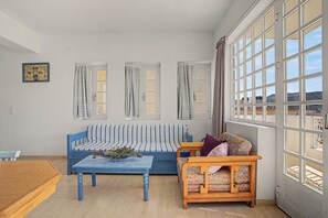Ein Wohnzimmer mit einem blauen Sofa, einem Holzstuhl, einem Couchtisch und einem großen Fenster mit Vorhängen.