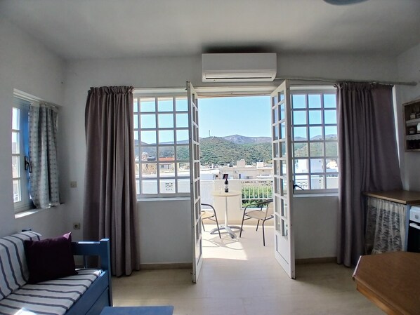 A room with a sofa, a table, and a view through open doors to a balcony.