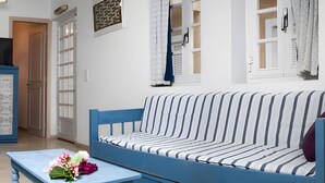 A room with a blue sofa, a small table with flowers, a framed picture on the wall, and a door leading to another room. - Apartment 'Memories' with Balcony, Wi-Fi and Air Conditioning (Palekastro)