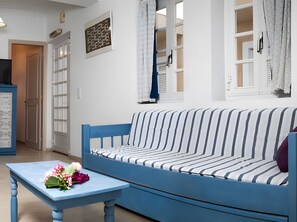 Una stanza con un divano blu, un tavolino con dei fiori, un quadro appeso al muro e una porta che dà su un'altra stanza.