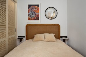 Een slaapkamer met een bed, een wandspiegel, een kunstwerk in een lijst en nachtkastjes.