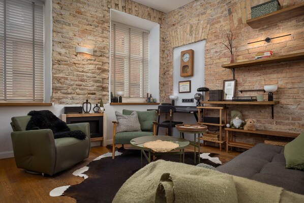 Een gezellige woonkamer met een bakstenen muur, een groene bank, een ronde salontafel en een open haard.