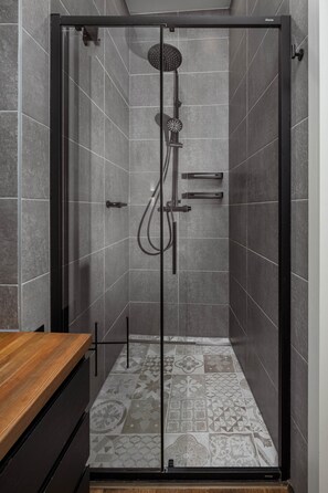 Een douche met een glazen deur, een handdouche en een bedieningspaneel aan de muur.