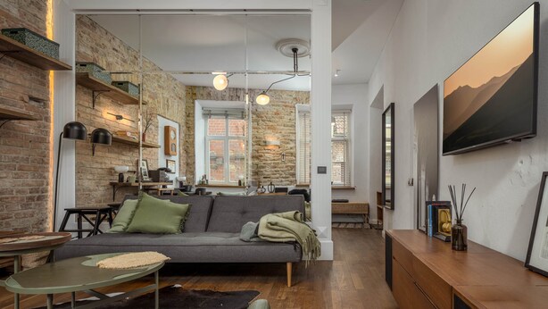 Un salón moderno con pared de ladrillo, un sofá gris, una mesa de centro de madera y un televisor en la pared.
