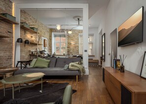 Een moderne woonkamer met een bakstenen muur, een grijze bank, een houten salontafel en een televisie aan de muur.