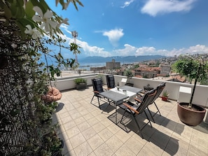 Une terrasse sur le toit, avec une table et des chaises, des plantes en pot et une vue sur la ville et la mer.