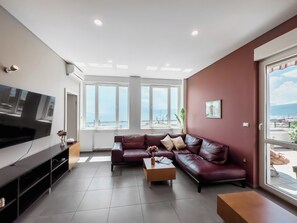 Ein modernes Wohnzimmer mit einem Ecksofa, einem Couchtisch, einem Flachbildfernseher und großen Fenstern mit Meerblick.