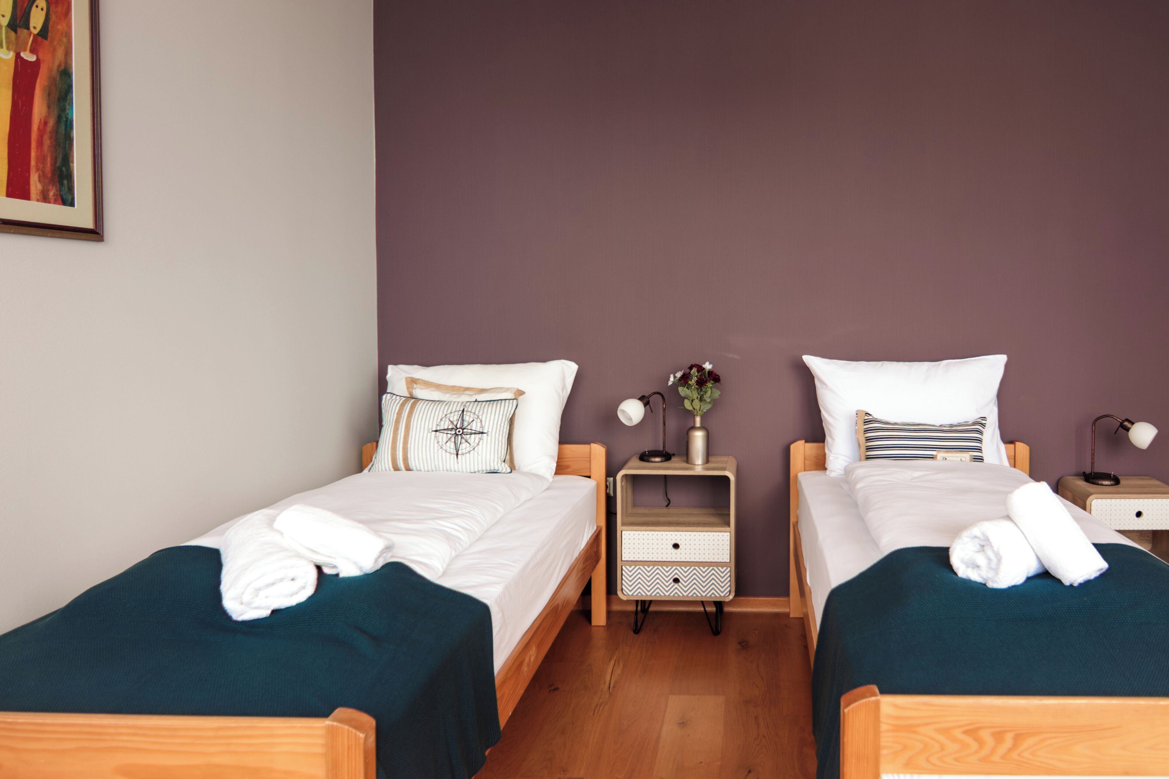 A double room with two beds, each with a pillow, a bedside table with a lamp, and a small drawer.