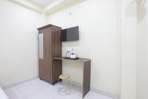 Une pièce comprenant un placard, un bureau avec une chaise, un téléviseur fixé au mur et un petit tabouret.