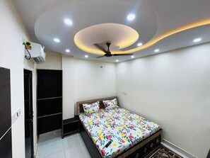 Un dormitorio con cama, ventilador de techo, luces empotradas, armario y unidad de aire acondicionado pequeña.