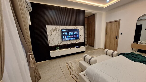 Ein modernes Schlafzimmer mit einem großen Bett, einem an der Wand montierten Fernseher, einem Holzschrank und einem Spiegel.