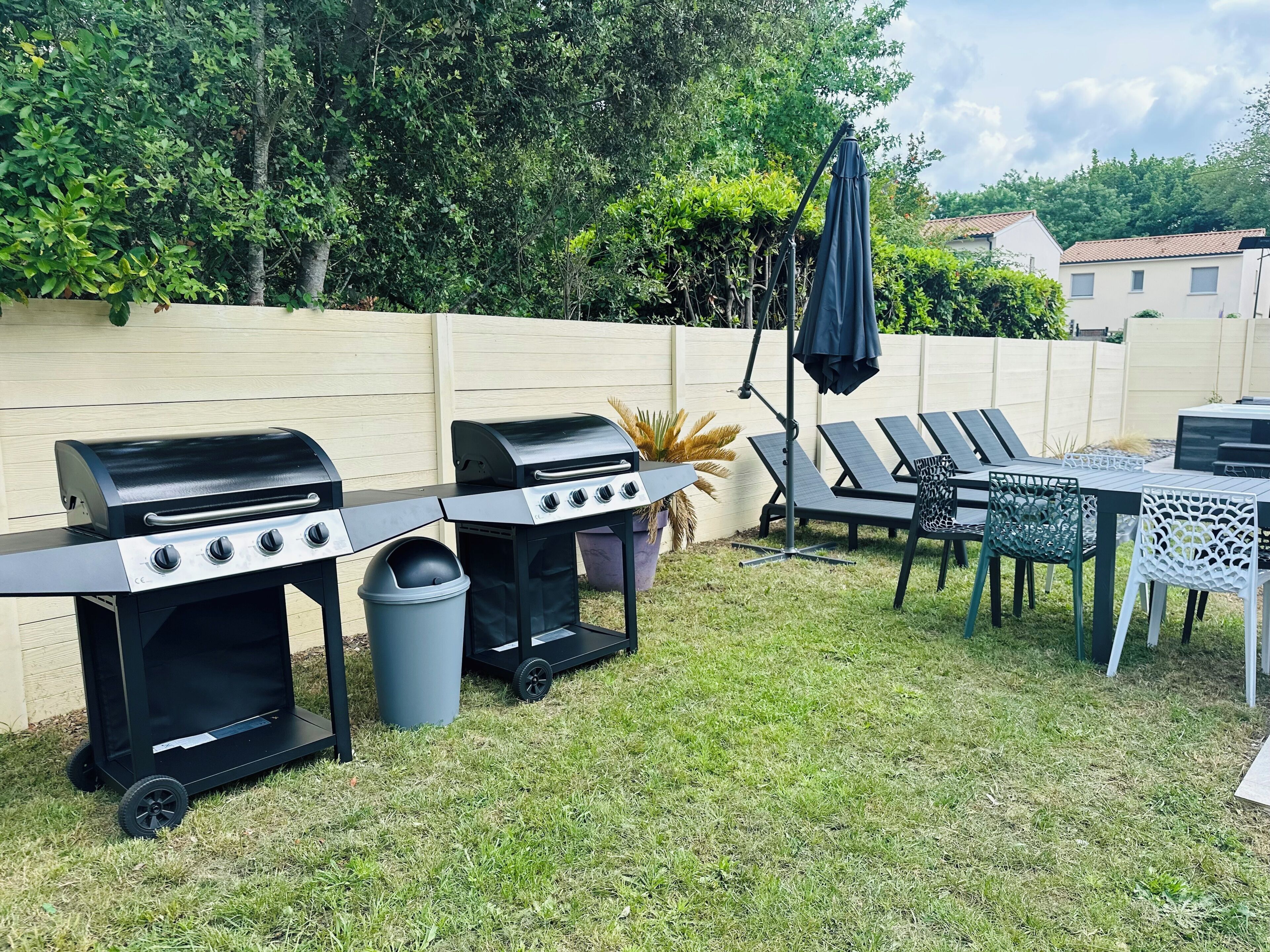 A backyard with two barbecue grills, a table with chairs, and a potted plant.