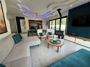 Ein modernes Wohnzimmer mit einer Couch, Sesseln, einem Couchtisch, einem Kamin und einem Fernseher.