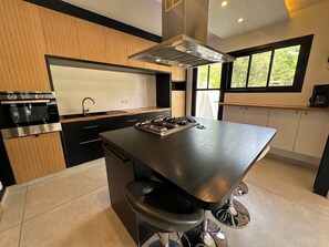 A modern kitchen with a central island, stainless steel appliances, and large windows. - Large 10-bedroom house - Jacuzzi - Garden - Near Bordeaux & Tram (Villenave-d'Ornon)
